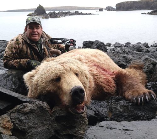 A hunter displaying his bear on rocks near a lake